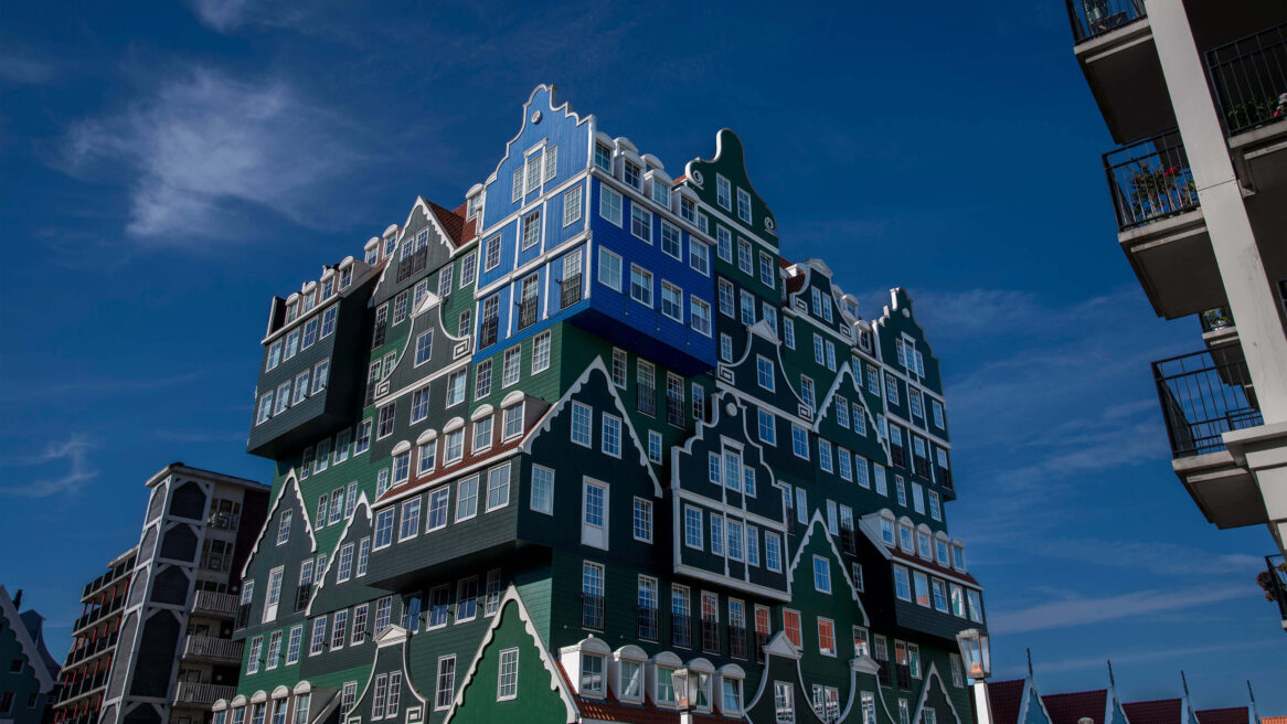 Inntel Hotel Zaandam. Op één huisje na zijn alle huisjes op de gevel groen. Het ene blauwe huisje staat voor het huisje van Monet. Hij schilderde in 1871 namelijk het schilderij La Maison Bleue, hierop is een blauw Zaans huisje te zien.